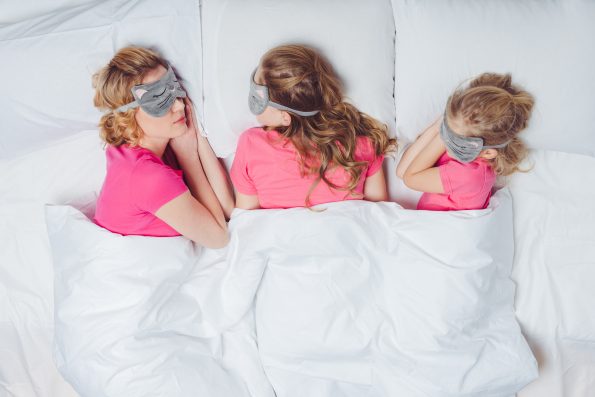 top view of mother and daughters with sleeping masks in shape of cat faces sleeping together in bed