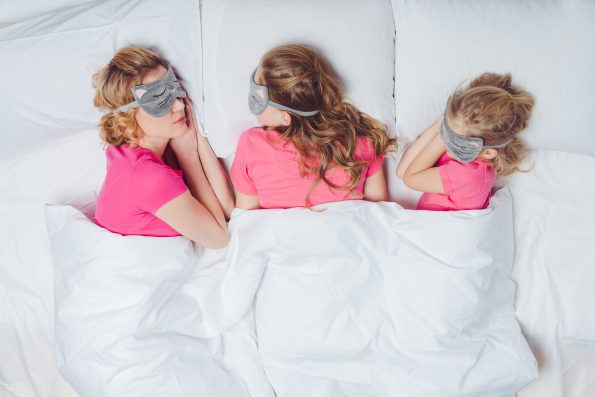 When to Know you are Oversleeping? - Navien Mate - Heated Mattress Pad | Thermal Blanket for Bed top view of mother and daughters with sleeping masks in shape of cat faces sleeping together in bed